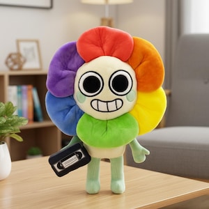 Könnte beinhalten: Ein Plüschblumen-Charakter mit einem lächelnden Gesicht, großen schwarzen Augen und einem Regenbogen-Blütenblatt-Design. Das Plüschtier hält eine kleine schwarze Kassette und hat grüne Arme und Beine. Das Spielzeug steht auf einem Holztisch.