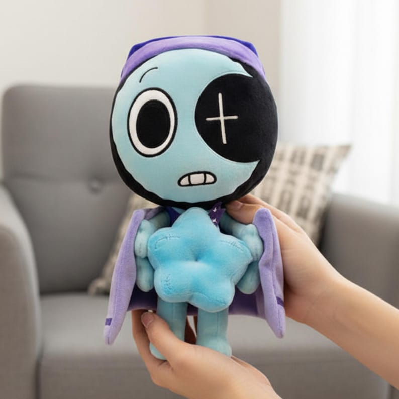 Pode incluir: Um brinquedo de pel&uacute;cia com um personagem azul com uma cabe&ccedil;a em forma de lua crescente, um olho grande e uma cruz. O personagem usa um bon&eacute; e capa roxos e segura uma estrela azul. O brinquedo &eacute; segurado por m&atilde;os.