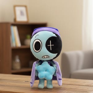 Könnte beinhalten: Eine Plüschpuppe mit hellblauem Gesicht, einem schwarz-weißen Auge und einem Halbmond-Design. Die Puppe trägt einen lila Umhang und hält einen blauen Stern. Die Puppe hat einen lila Hut und einen blauen Körper.