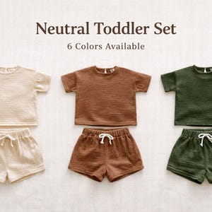 May include: A neutral toddler set in three colors: cream, brown, and olive green. Each set includes a short-sleeved top and matching shorts with a drawstring waist. The text "Neutral Toddler Set" and "6 Colors Available" are displayed.