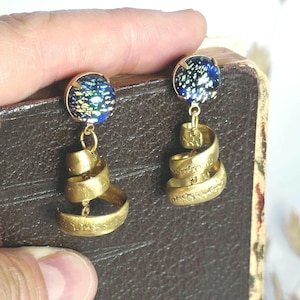 Peut inclure: Une paire de boucles d'oreilles pendantes composée d'un clou circulaire avec un cabochon en verre bleu foncé aux reflets irisés, relié à un élément en spirale en métal doré avec une finition texturée martelée et un design enroulé.