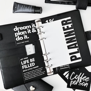 Könnte beinhalten: Ein schwarzer Planer mit sechs Ringen und weißen Seiten mit dem Text PLANNER, dream it. plan it & do it. sowie LET YOUR LIFE BE FILLED WITH LITTLE THINGS. Enthält eine schwarze Cremetube und eine schwarze Karte mit dem Text Coffee person.