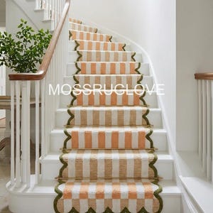May include: Staircase with white risers and a curved wooden handrail. The steps are adorned with striped stair runners in shades of orange, white, and tan. The runners have a scalloped edge with a green border. The text "MOSSRUGLOVE" is visible.