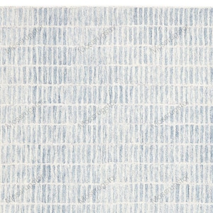Puede incluir: Una alfombra rectangular con un patrón geométrico texturizado. El diseño presenta rayas verticales en diferentes tonos de azul y blanco, creando una estética moderna y visualmente atractiva. La alfombra es adecuada para salones, dormitorios o entradas.
