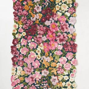 May include: A rectangular rug with a floral pattern. The rug features a dark teal background with a dense arrangement of flowers in shades of pink, yellow, and burgundy. The edges of the rug are scalloped.
