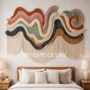 May include: A large, horizontal wall hanging featuring layered, wavy bands of tufted fabric in shades of rust, dusty pink, sage green, cream, and charcoal gray. The piece includes a long, cream-colored fringe along the bottom edge with MUSSRUGLOVE text.