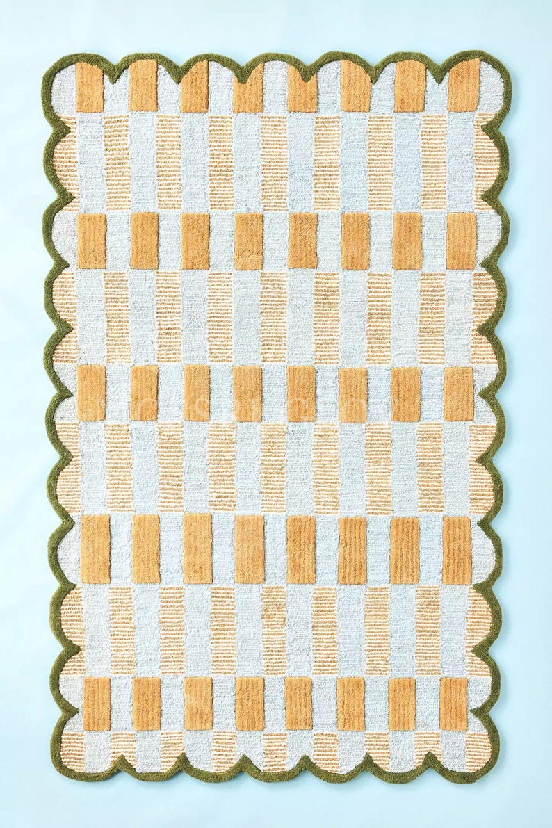 Puede incluir: Una alfombra rectangular con un patr&oacute;n repetitivo de rayas verticales blancas y doradas, intercaladas con bloques rectangulares dorados. La alfombra tiene un borde verde festoneado, creando un borde decorativo. La alfombra est&aacute; sobre una superficie azul claro.