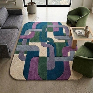 May include: A rectangular area rug featuring a geometric pattern of interlocking rounded lines in shades of teal, deep green, purple, and cream. The rug has a textured, tufted surface and rounded corners, creating a bold, colorful visual focal point.