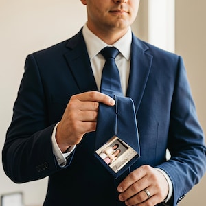 May include: A navy blue suit jacket worn over a white dress shirt and a matching navy blue necktie. The necktie features a square-shaped, custom-printed photograph of two people displayed prominently on the front surface of the fabric.