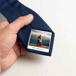 May include: A dark blue necktie with a textured fabric finish featuring a square photo print on the underside. The photo depicts two people standing together in a mountainous landscape with the text Together is my favourite place to be.