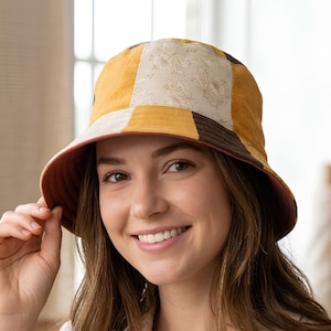 May include: A patchwork bucket hat with a yellow, brown, and cream floral pattern. The hat has a brown brim and a matching interior. The hat is a stylish accessory for sun protection or fashion.