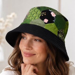 May include: A patchwork bucket hat with a black brim and a crown featuring green and black geometric patterns, and floral accents. The hat is worn by a person in a white shirt.