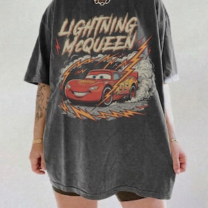 May include: Dark gray t-shirt featuring Lightning McQueen from the movie Cars. The graphic shows the red race car with the number 95, surrounded by lightning bolts and the text "Lightning McQueen".