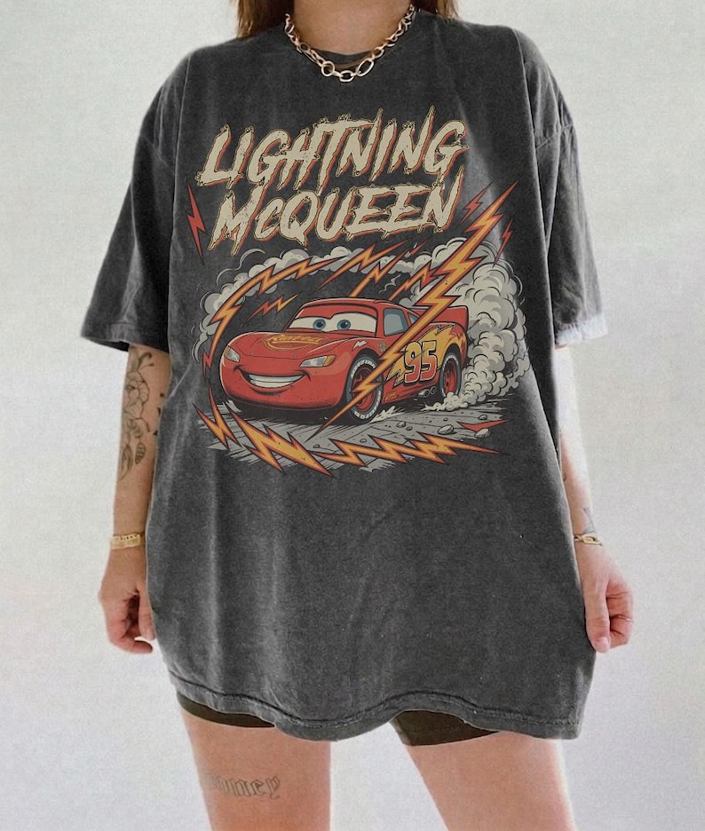 May include: Dark gray t-shirt featuring Lightning McQueen from the movie Cars. The graphic shows the red race car with the number 95, surrounded by lightning bolts and the text "Lightning McQueen".