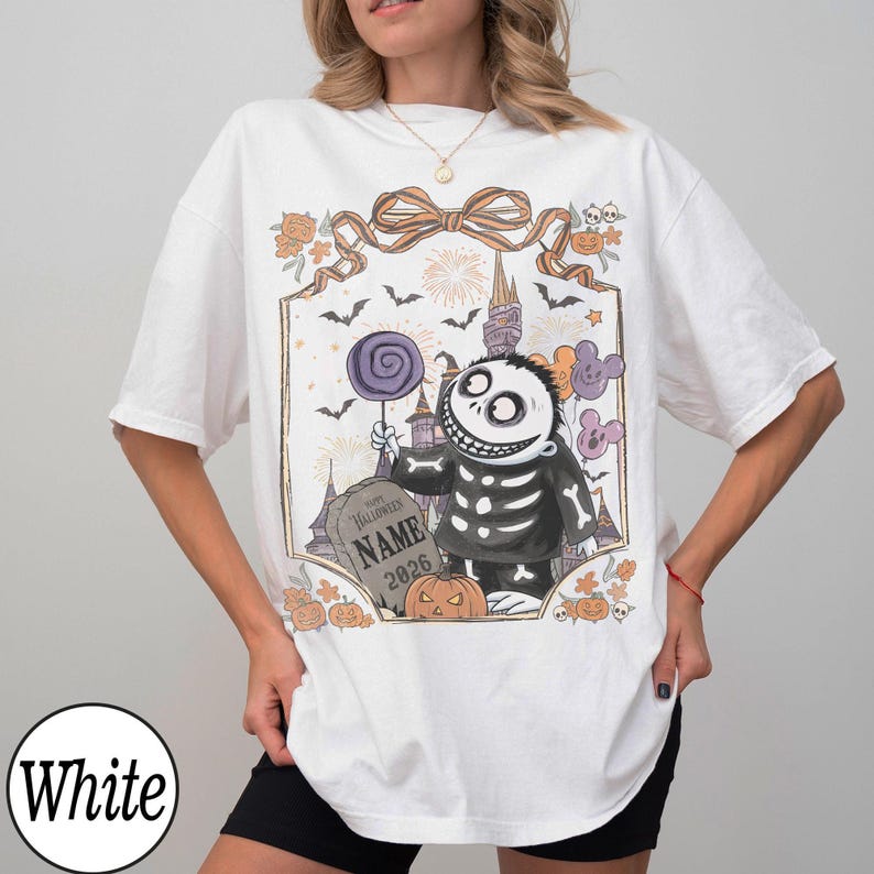 K&ouml;nnte beinhalten: Wei&szlig;es T-Shirt mit einem Halloween-Motiv. Das Design zeigt eine Skelettfigur, die einen Lolli und Luftballons h&auml;lt, mit einem Grabstein mit der Aufschrift "NAME 2026". Das Motiv ist mit Flederm&auml;usen, K&uuml;rbissen und Feuerwerk umrahmt.