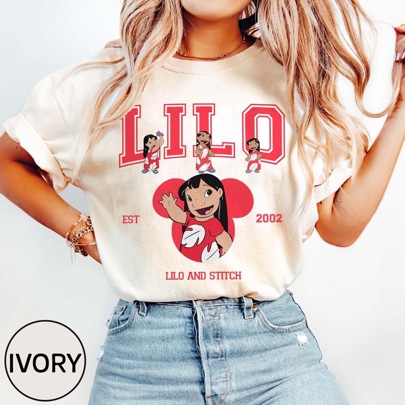 May include: Ivory-colored t-shirt featuring the word "LILO" in red block letters with three small character illustrations above. Below, a large red Mickey Mouse-shaped graphic with a character illustration and the text "LILO AND STITCH". The year "2002" is also displayed.