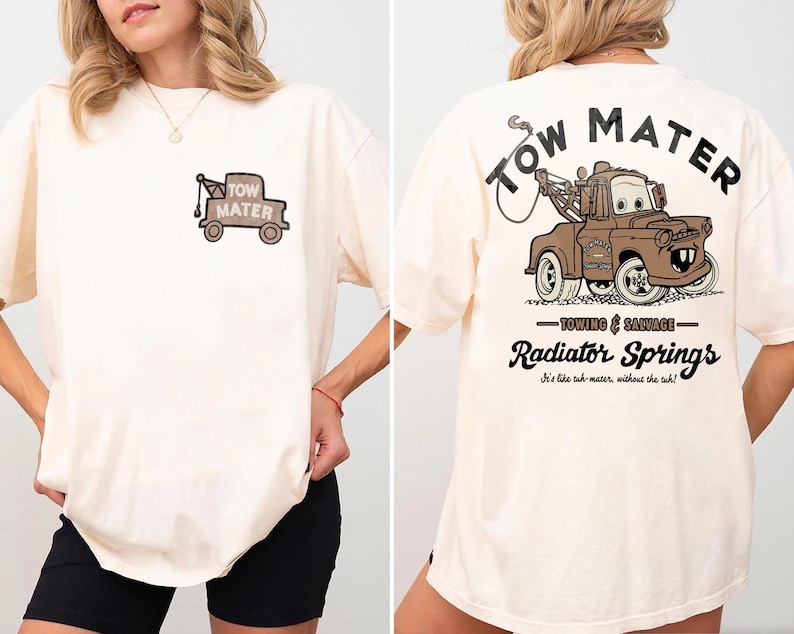 May include: An off-white t-shirt featuring a small graphic of a brown tow truck on the front left chest. The back displays a large brown tow truck graphic with the text Tow Mater, Towing & Salvage, Radiator Springs, and It's like tuh-mater, without the tuh.