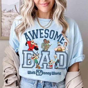 May include: Light blue t-shirt with the words "AWESOME DAD" in navy blue block letters, featuring Disney characters. The shirt also includes the text "Walt Disney World" and a Disney logo.