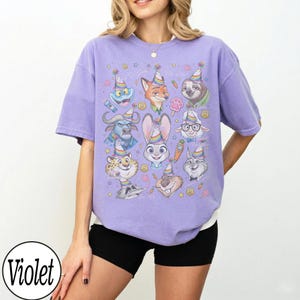 May include: A violet-colored t-shirt featuring a colorful graphic of cartoon animal characters wearing party hats. The graphic includes a bunny, fox, sloth, and other animals. The word "Violet" is in a white circle in the bottom left.