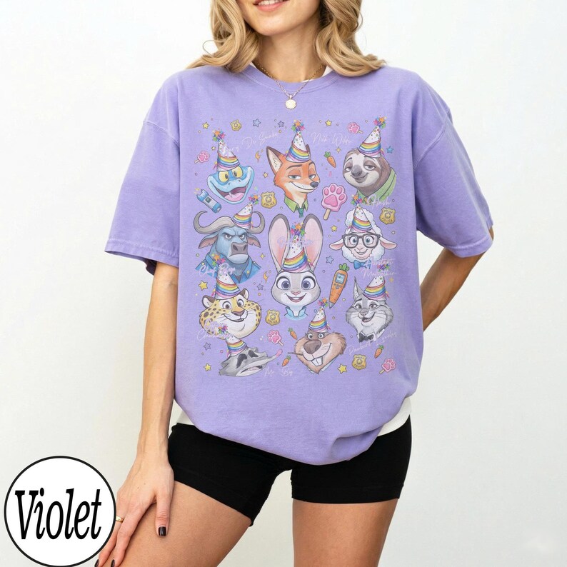 May include: A violet-colored t-shirt featuring a colorful graphic of cartoon animal characters wearing party hats. The graphic includes a bunny, fox, sloth, and other animals. The word "Violet" is in a white circle in the bottom left.