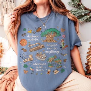 Peut inclure: T-shirt bleu avec un motif graphique color&eacute;. Le motif comprend les phrases "Hakuna Matata", "Anyone can be anything" et "Adventure is out there". Les illustrations pr&eacute;sentent des animaux, un arbre et un v&eacute;hicule de safari.