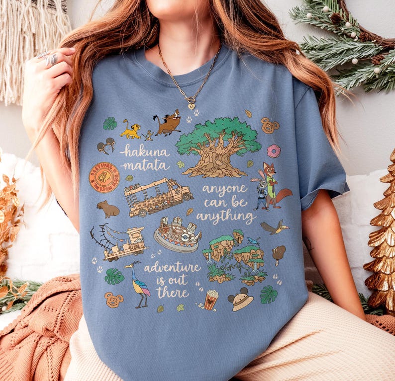 Peut inclure: T-shirt bleu avec un motif graphique color&eacute;. Le motif comprend les phrases "Hakuna Matata", "Anyone can be anything" et "Adventure is out there". Les illustrations pr&eacute;sentent des animaux, un arbre et un v&eacute;hicule de safari.
