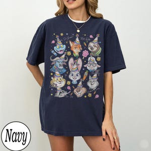 May include: Navy blue t-shirt featuring a colorful graphic of cartoon animal characters wearing party hats. The design includes a variety of animals, such as a fox, sloth, and bunny, with the text "Happy Birthday" and "Nick Wilde".