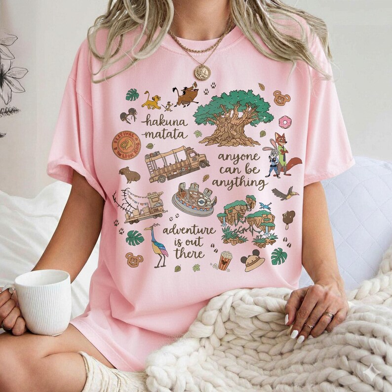 Peut inclure: T-shirt rose clair avec un motif graphique color&eacute;. Le motif comprend les mots "Hakuna Matata", "Anyone can be anything" et "Adventure is out there", ainsi que des animaux de dessins anim&eacute;s et d'autres illustrations.