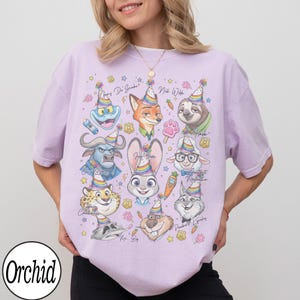 May include: A light purple t-shirt featuring cartoon characters from Zootopia, each wearing a party hat. The characters include Judy Hopps, Nick Wilde, and Flash. The shirt has the word "Orchid" in a white circle at the bottom.