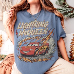 May include: A light blue t-shirt featuring Lightning McQueen from the Cars movie. The graphic shows the red race car with the number 95, surrounded by lightning bolts and the text "Lightning McQueen".