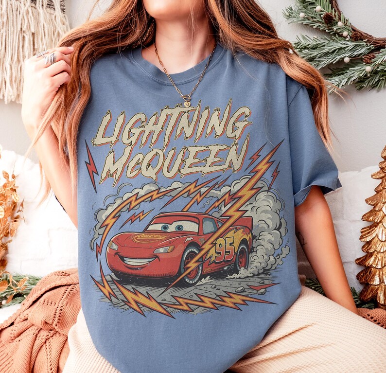 May include: A light blue t-shirt featuring Lightning McQueen from the Cars movie. The graphic shows the red race car with the number 95, surrounded by lightning bolts and the text "Lightning McQueen".
