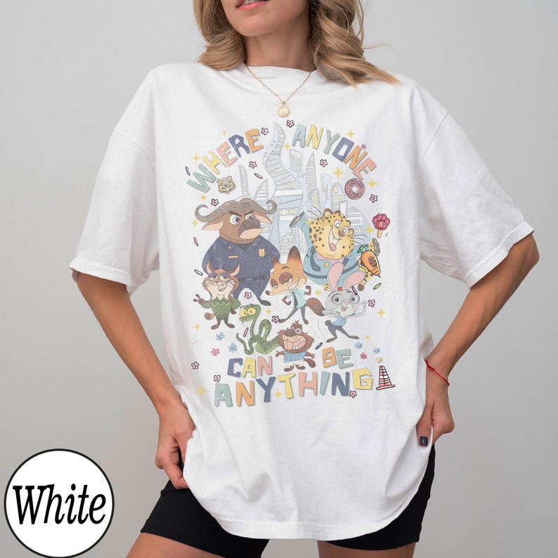 May include: White t-shirt featuring a colorful graphic of characters from the animated film "Zootopia." The design includes the text "WHERE ANYONE CAN BE ANYTHING" in a playful font, with various animal characters.