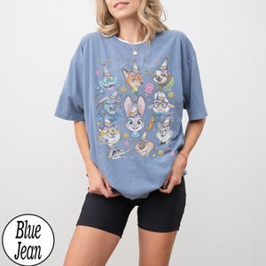 May include: A blue jean t-shirt featuring a colorful graphic of cartoon animal characters wearing party hats. The shirt has a crew neck and short sleeves. The text "Blue Jean" is in a white circle at the bottom left.