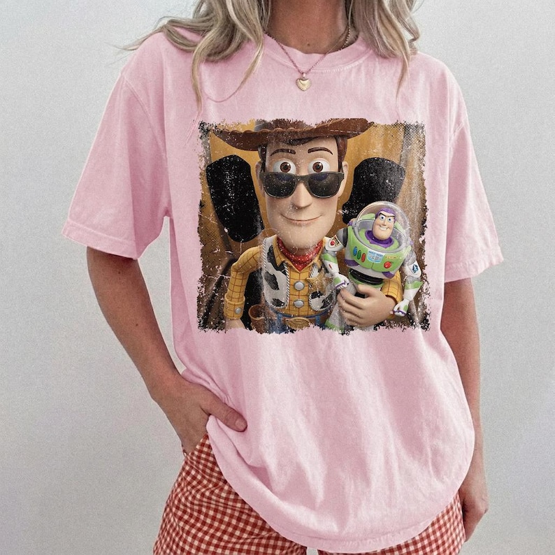 Puede incluir: Camiseta rosa claro con un gr&aacute;fico de Woody y Buzz Lightyear de Toy Story. Woody lleva gafas de sol y un sombrero de vaquero. Buzz Lightyear est&aacute; en su traje espacial. El gr&aacute;fico tiene un aspecto vintage.