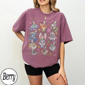 May include: Berry-colored t-shirt featuring cartoon characters from Zootopia wearing party hats. The shirt has a crew neck and short sleeves. The word "Berry" is printed in a white circle at the bottom left.