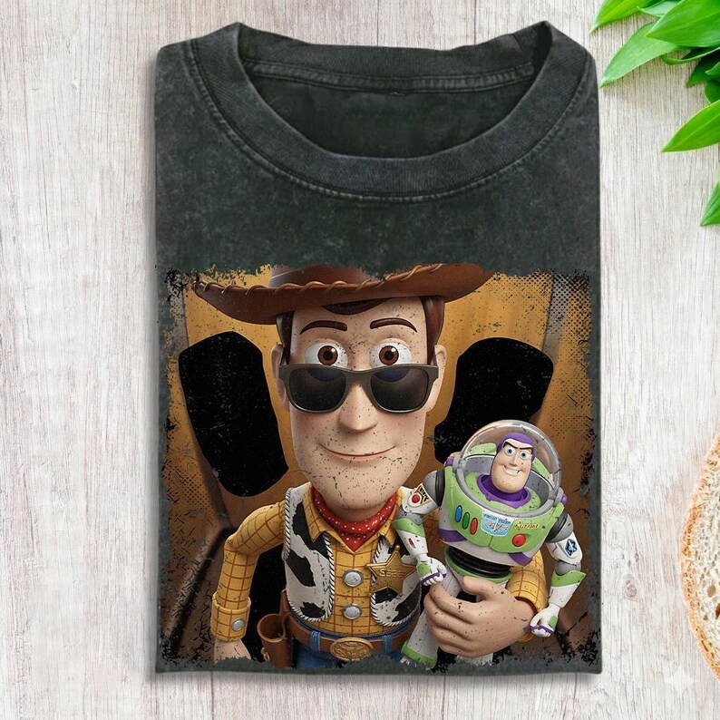Puede incluir: Camiseta gris oscuro con un dise&ntilde;o de Woody y Buzz Lightyear de Toy Story. Woody lleva gafas de sol, sombrero de vaquero y placa de sheriff. Buzz Lightyear est&aacute; en su traje espacial. La camiseta tiene un aspecto desgastado.