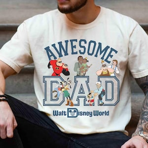 May include: Cream-colored t-shirt with the words "AWESOME DAD" in blue block letters, featuring Disney characters. The phrase "Walt Disney World" is printed below the word "DAD".