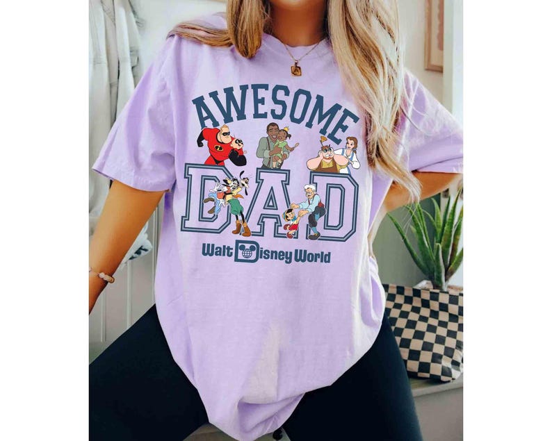 May include: A light purple t-shirt with the words "AWESOME DAD" in a blue and white collegiate style font. The shirt features Disney characters and the text "Walt Disney World" below the word "DAD".