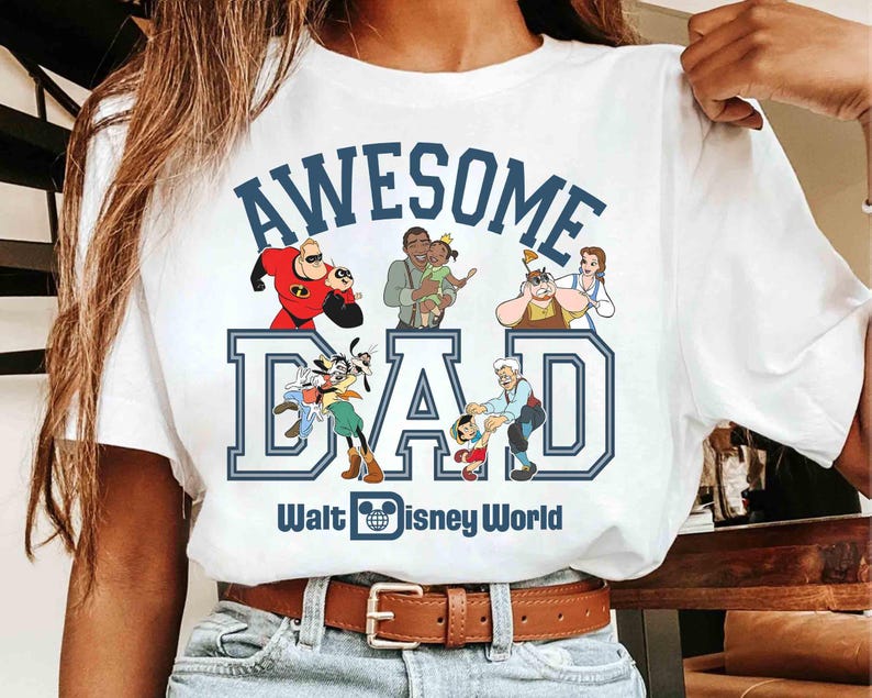 May include: White t-shirt with a blue graphic that reads "AWESOME DAD" with Disney characters and the text "Walt Disney World". The shirt features a brown leather belt and blue jeans.