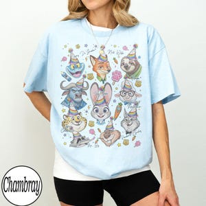 May include: Light blue t-shirt featuring cartoon characters from Zootopia wearing party hats. The shirt includes characters like Judy Hopps, Nick Wilde, and Flash. The word "Chambray" is printed on the bottom left of the shirt.