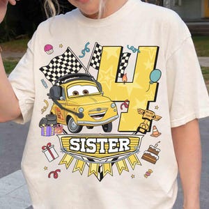 K&ouml;nnte beinhalten: Ein cremefarbenes T-Shirt mit einem Grafikdruck eines gelben Cartoon-Autos mit Kopfh&ouml;rern, einer gro&szlig;en gelben Zahl 4, Zielflaggen, einem Piston-Cup-Pokal und dem Wort SISTER. Das Design enth&auml;lt bunte Party-Elemente wie Geschenke, Kuchen und Luftballons.