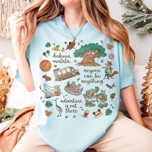 Peut inclure: T-shirt bleu clair avec un motif graphique color&eacute;. Le motif comprend les phrases "hakuna matata", "anyone can be anything" et "adventure is out there". Le motif comprend des personnages de dessins anim&eacute;s et d'autres &eacute;l&eacute;ments th&eacute;matiques.