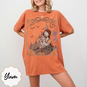 K&ouml;nnte beinhalten: Orangefarbenes T-Shirt mit einer Grafik einer Figur aus The Nightmare Before Christmas. Das Design beinhaltet einen Grabstein mit dem Text "Halloween Name 2026" und andere Halloween-Elemente. Das Shirt hat kurze &Auml;rmel und eine lockere Passform.