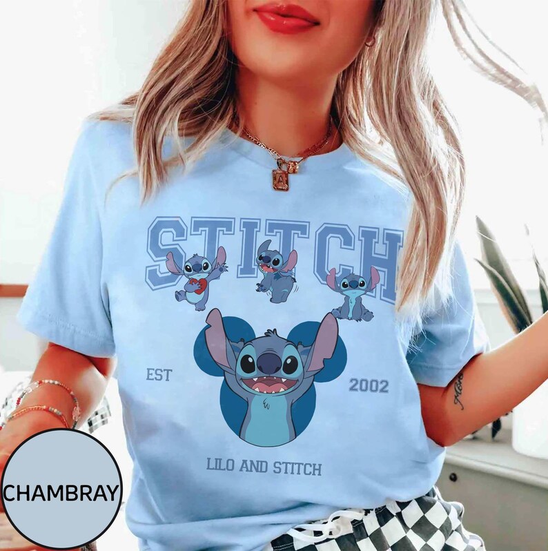 May include: Light blue t-shirt featuring the word "STITCH" in a collegiate font above four cartoon Stitch characters. The shirt also includes the text "EST 2002" and "LILO AND STITCH".
