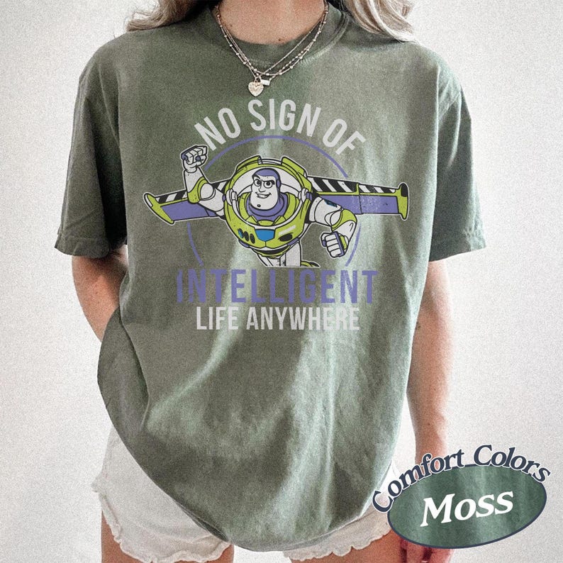 K&ouml;nnte beinhalten: Ein moosgr&uuml;nes T-Shirt mit einem Buzz Lightyear-Motiv und dem Text "NO SIGN OF INTELLIGENT LIFE ANYWHERE". Das Design zeigt eine kreisf&ouml;rmige Grafik von Buzz Lightyear. Das Shirt ist mit "Comfort Colors Moss" gekennzeichnet.