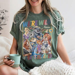 May include: Green t-shirt with a colorful graphic featuring cartoon animal characters and the text "WE'RE WILD" and "W CAN'T BE TAMED". The shirt has a crew neck and short sleeves.