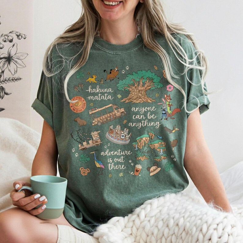 Peut inclure: T-shirt vert avec un graphisme color&eacute; repr&eacute;sentant des personnages et des phrases d'un film d'animation populaire. Le motif comprend les phrases "hakuna matata", "anyone can be anything" et "adventure is out there".