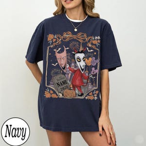 K&ouml;nnte beinhalten: Marineblaues T-Shirt mit einem Halloween-Motiv. Das Design zeigt eine Figur in einem roten Anzug, einen Grabstein mit dem Text "NAME 2026" und andere gruselige Elemente. Das T-Shirt hat kurze &Auml;rmel und einen Rundhalsausschnitt.