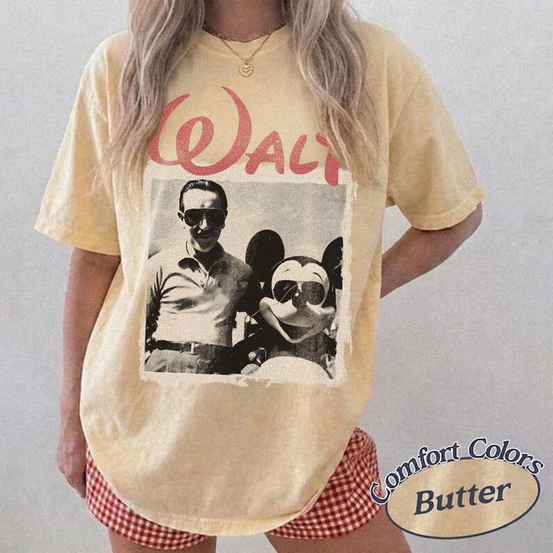 May include: Butter-colored t-shirt featuring a vintage black and white image of Walt Disney and Mickey Mouse. The word "Walt" is printed in red above the image. The shirt is a Comfort Colors brand.