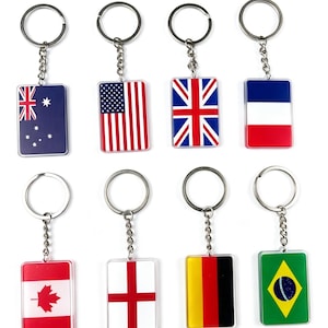 Puede incluir: Una colección de llaveros rectangulares con banderas de varios países. Las banderas incluyen Estados Unidos, Reino Unido, Francia, Australia, Canadá, Inglaterra, Alemania y Brasil. Cada llavero tiene un anillo y una cadena plateados.
